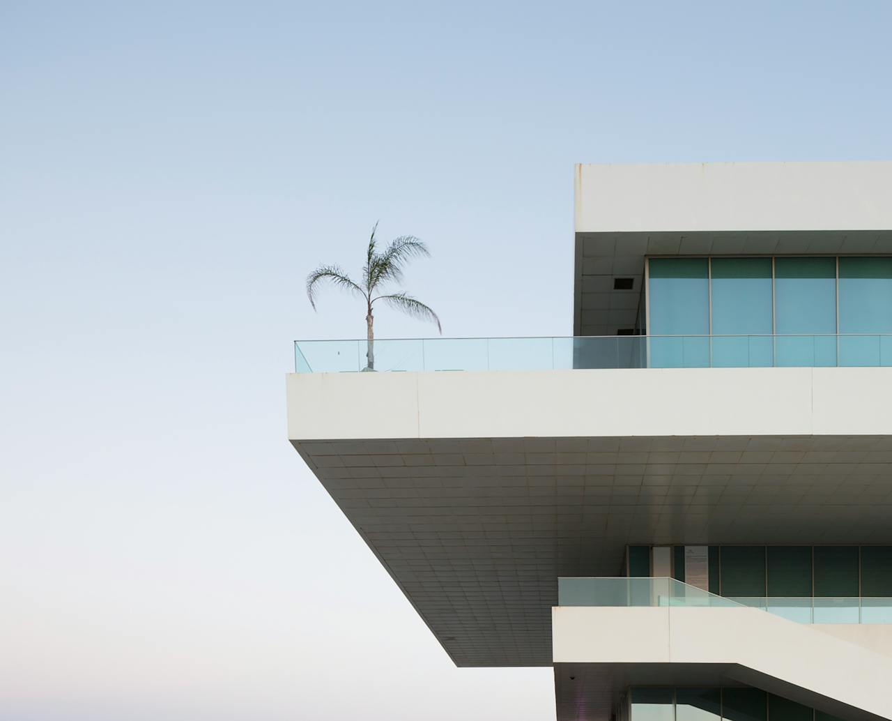 Contemporary building with glass balconies and palm tree against a clear sky.